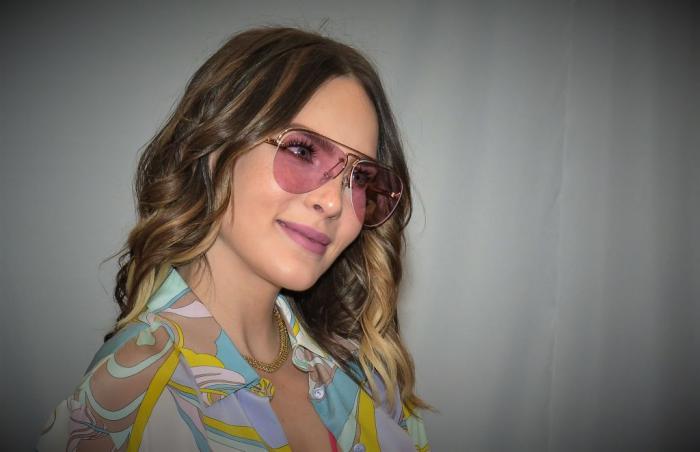 Belinda poartă ochelari de soare și are părul lung, ondulat