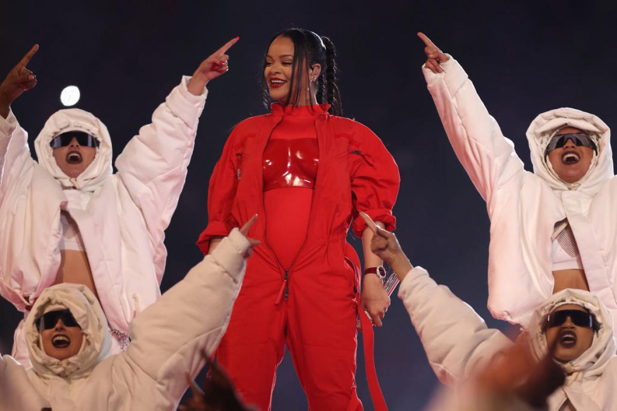Rihanna poartă un costum roșu și are părul prins în coadă