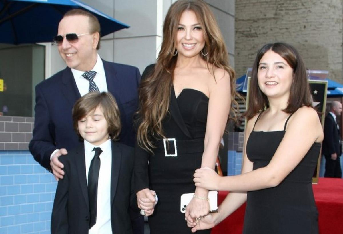 Thalia poartă o rochie neagră fără mâneci și stă alături de familie