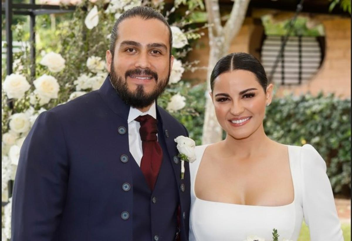 Andres Tovar poartă un costum negru și Maite Perroni poartă o rochie albă de mireasă