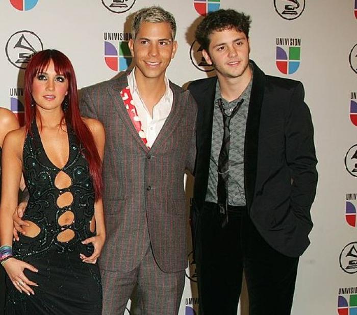 Dulce Maria poartă o rochie neagră decupată, Christian Chavez poartă un costum gri, iar Christopher Uckermann poartă un costum negru și cravată