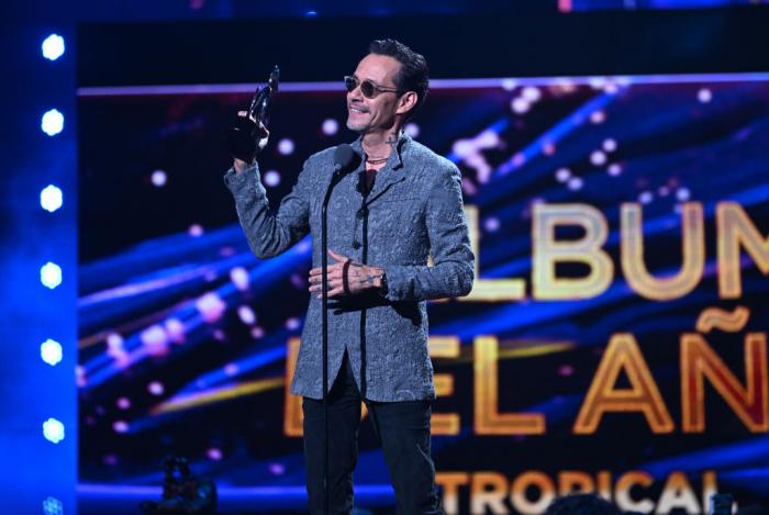 Marc Anthony poartă un costum și ține premiul în mână pe scenă