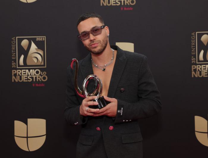 Prince Royce poartă un sacou negru și ochelari de soare și își ține premiul în mână pe covorul roșu