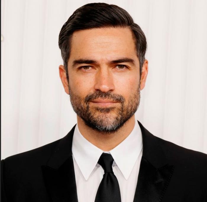 Alfonso Herrera poartă o cămașă albă, cravată neagră și sacou negru