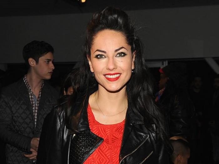 Barbara Mori poartă un tricou roșu, o geacă neagră și zâmbește