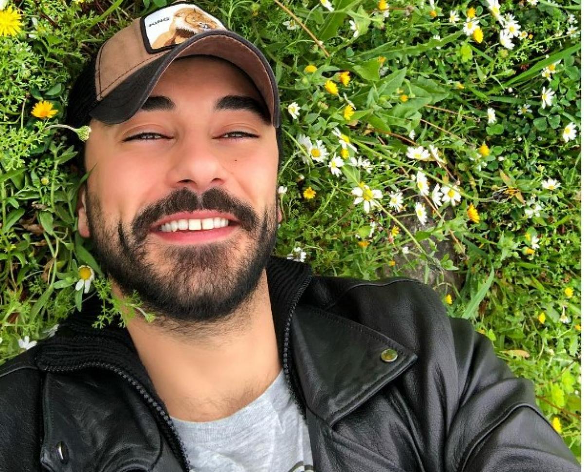 Gökhan Alkan poartă un tricou gri și șapcă și zâmbește