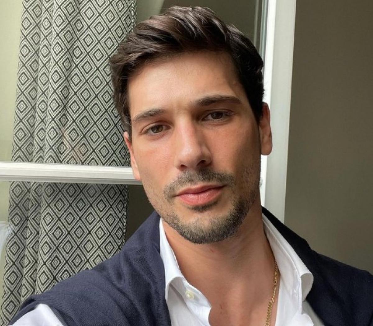 Deniz Aktaș poartă o cămașă albă și un pulover închis la culoare