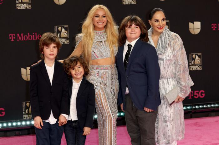 Paulina Rubio poartă o fustă aurie și un top scurt în același model și stă alături de mama sa și copiii