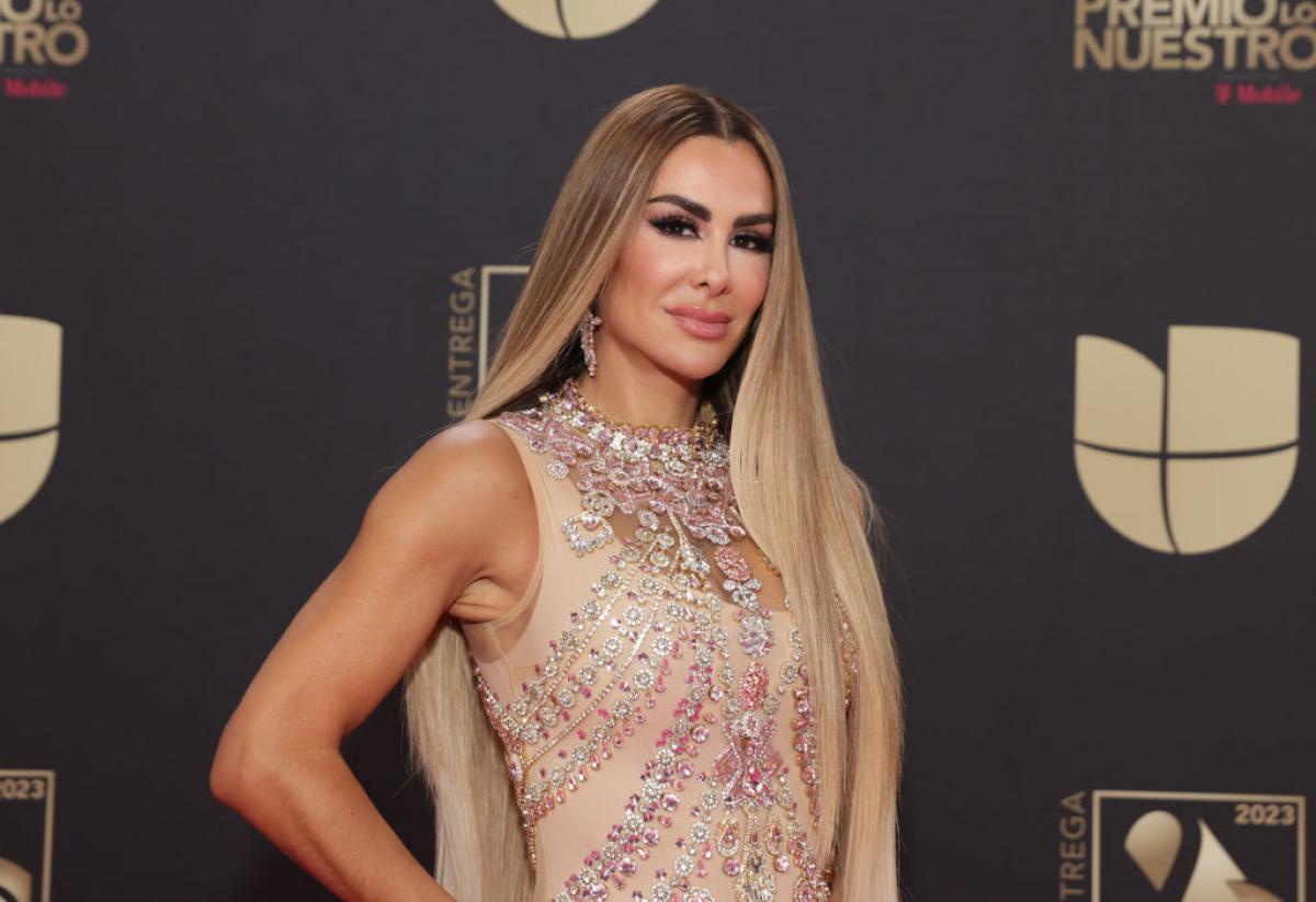 Ninel Conde poartă o rochie de gală, fără mâneci și are părul lung, desprins