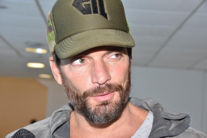 Julián Gil poartă o șapcă verde și are barbă