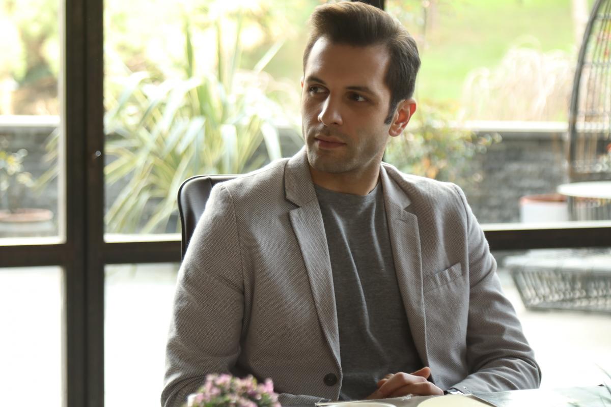 Çağrı Çıtanak poartă un tricou gri și un sacou deschis la culoare