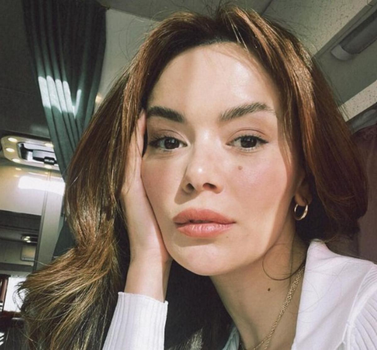 Seray Kaya poartă părul lung desprins și își ține mâna dreaptă pe față