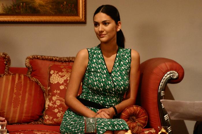 Bergüzar Korel poartă o rochie verde cu buline albe, fără mâneci. Are părul prins în coadă