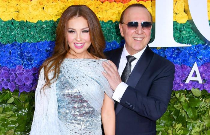 Thalia poartă o rochie gri și stă lângă Tommy Mottola. Zâmbesc