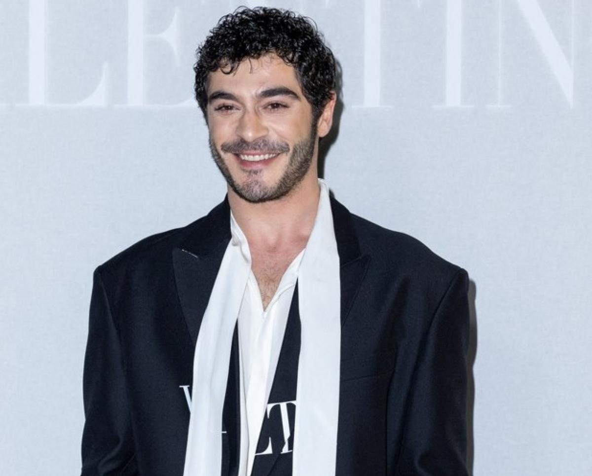 Burak Deniz poartă un sacou negru și o eșarfă albă