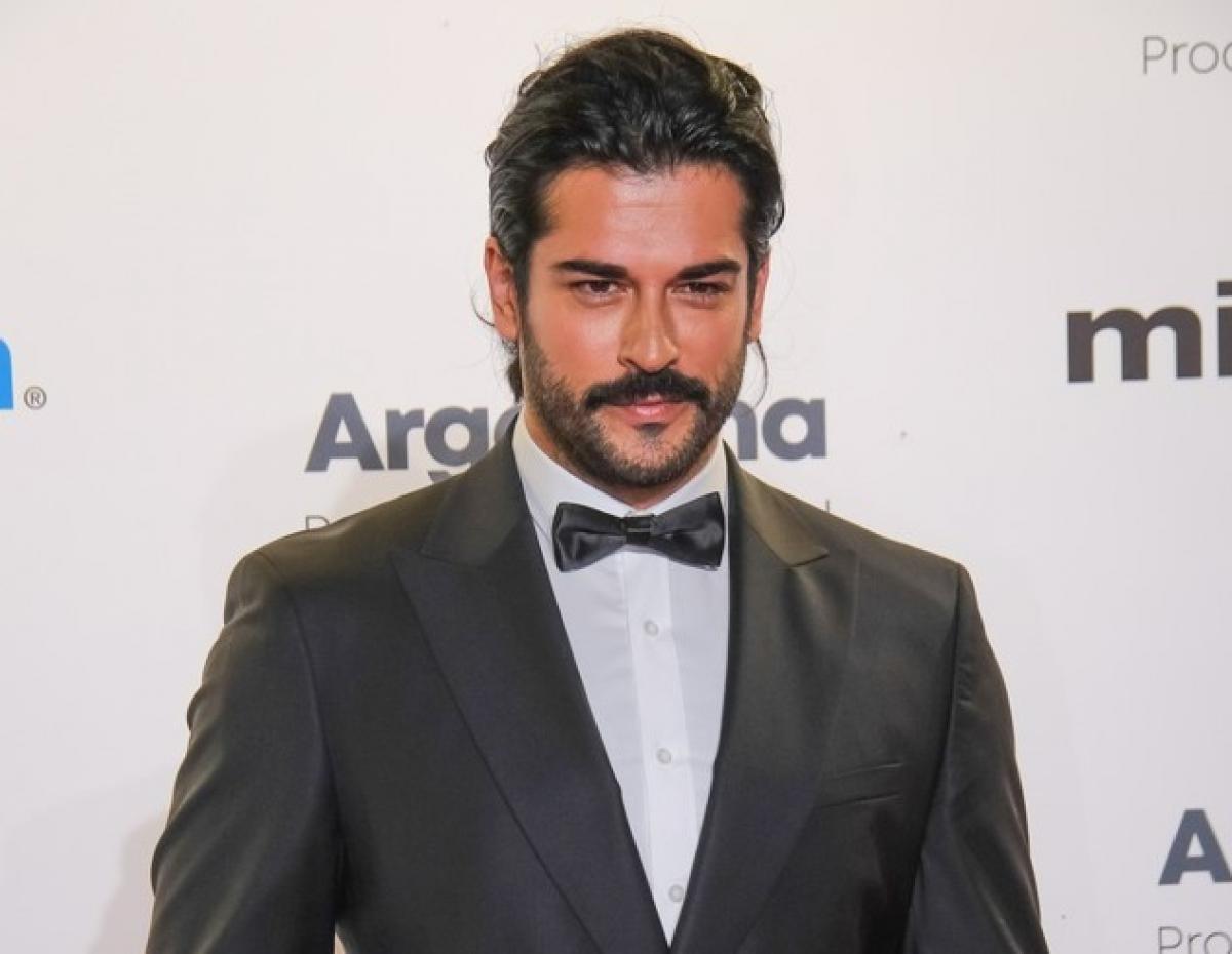 Burak Özçivit poartă o cămașă albă și sacou negru și are mustață