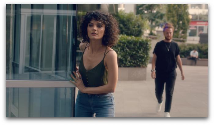 Nazlı Senem Ünal poartă un maiou negru, are părul scurt și ondulat și stă în spatele unei clădiri