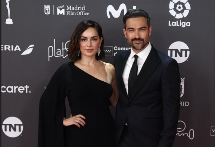 Alfonso Herrera poartă un costum negru și stă lângă Ana de la Reguera care poartă o rochie neagră cu un umăr gol