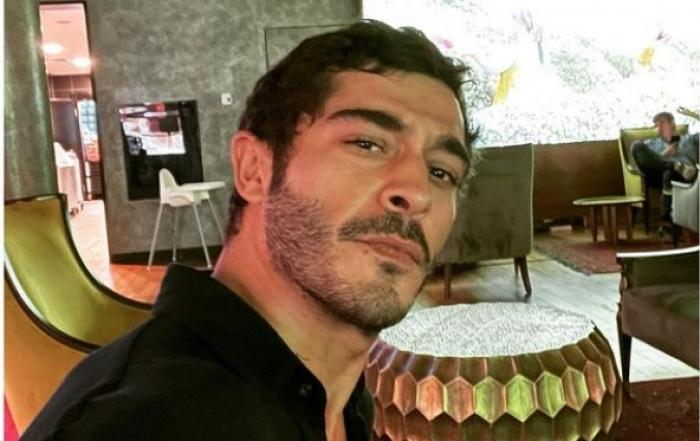 Burak Deniz poartă o cămașă neagră deschisă la gât