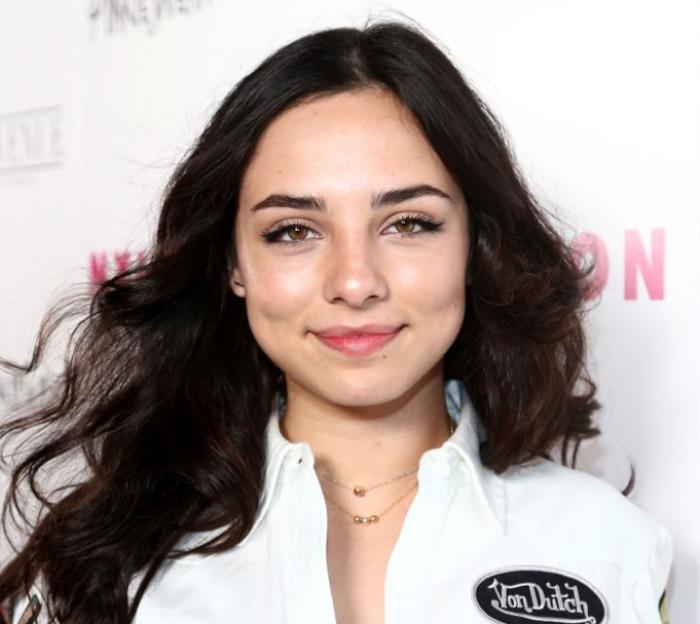Fiona Palomo poartă o bluză albă și părul lung, desprins
