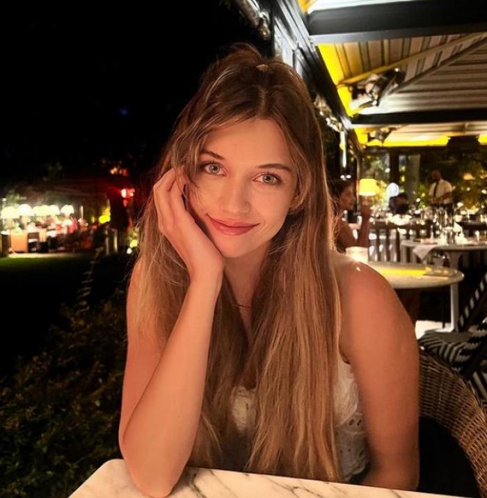 Afra Saraçoğlu poartă părul lung desprins și își ține mâna dreaptă la obraz