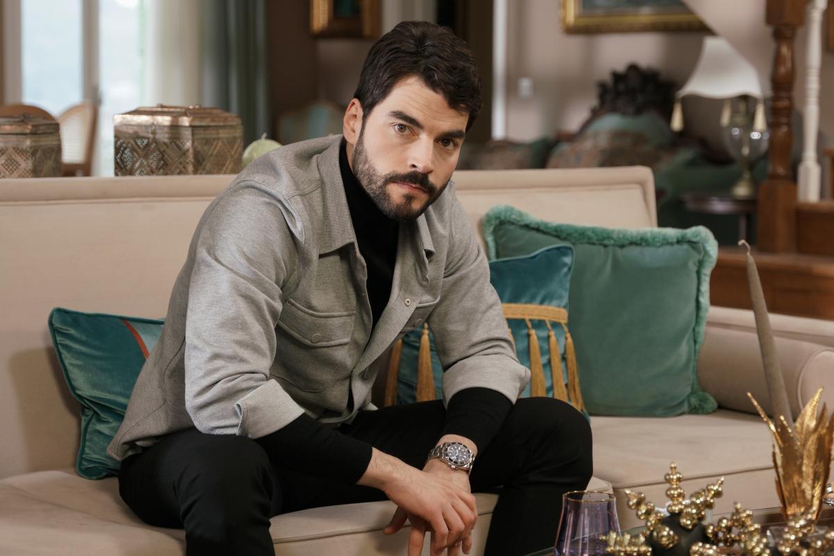 Akın Akınözü poartă o maletă neagră și un sacou gri