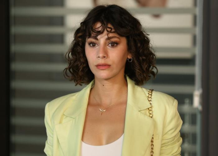 Tuğçe Açıkgöz poartă un tricou alb și un sacou galben