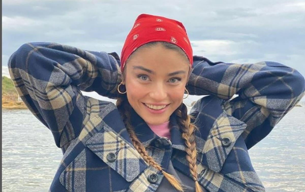 Ayça Ayşin Turan poartă o cămașă în carouri și are părul prins într-o coadă îmlpletită