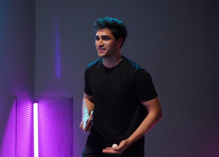 Mert Ramazan Demir poartă un tricou negru și pantaloni de aceeași culoare pe un fundal închis la culoare