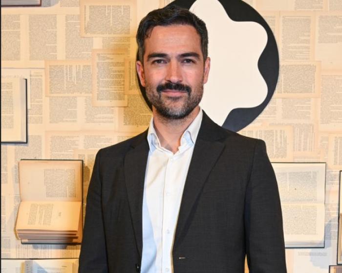 Alfonso Herrera poartă o cămașă albă și un sacou negru și are mustață