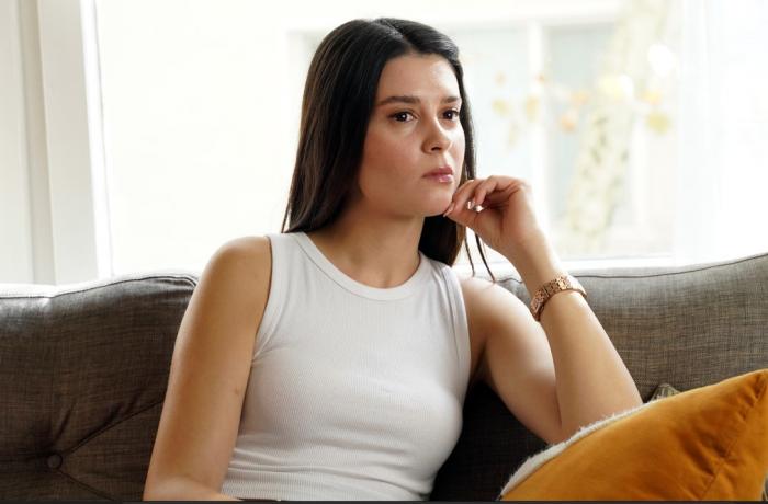 Buçe Buse Kahraman poartă un maiou alb și părul lung, desprins și ține mâna stângă în dreptul bărbiei