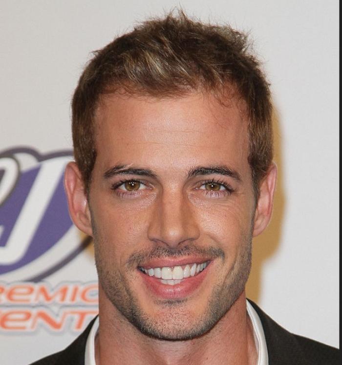 William Levy poartă o cămașă albă și un sacou negru și zâmbește