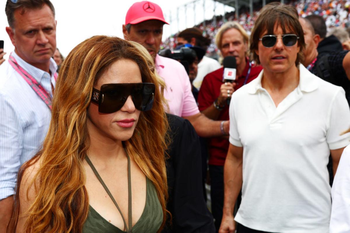 Shakira poartă un body verde, părul desprins și ochelari negri de soare și Tom Cruise poartă un tricou alb și ochelari negri de soare