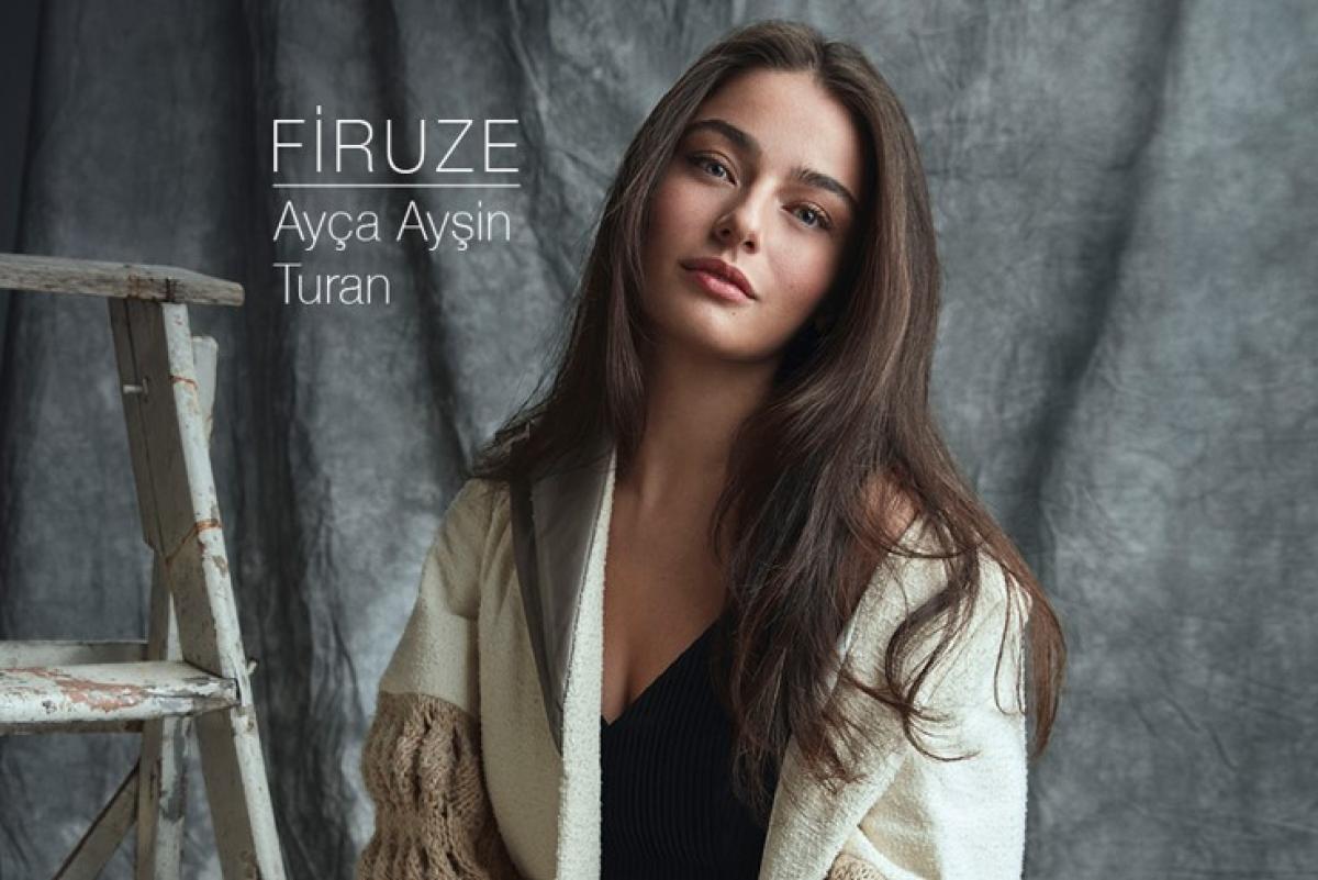 Ayça Ayşin Turan poartă un maiu negru și un pulover deschis la culoare