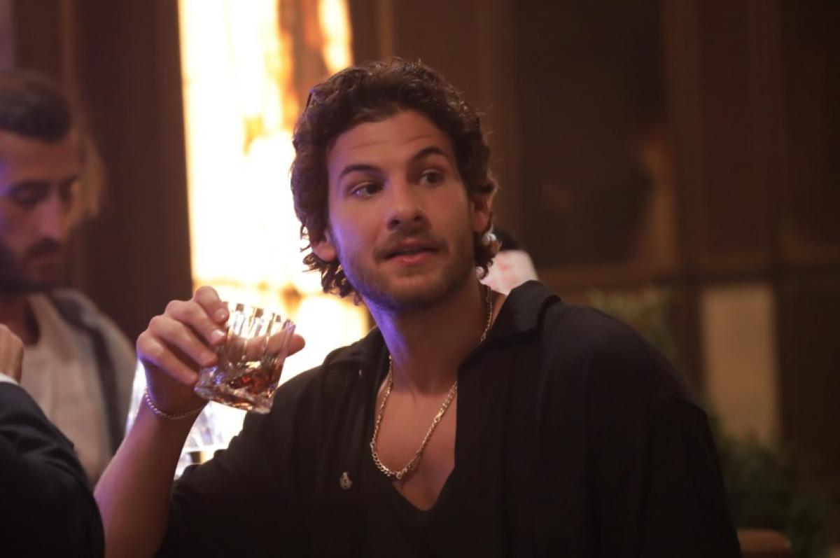 Mustafa Mert Koç poartă o cămașă neagră cu mâneci lungi și ține un pahar în mână