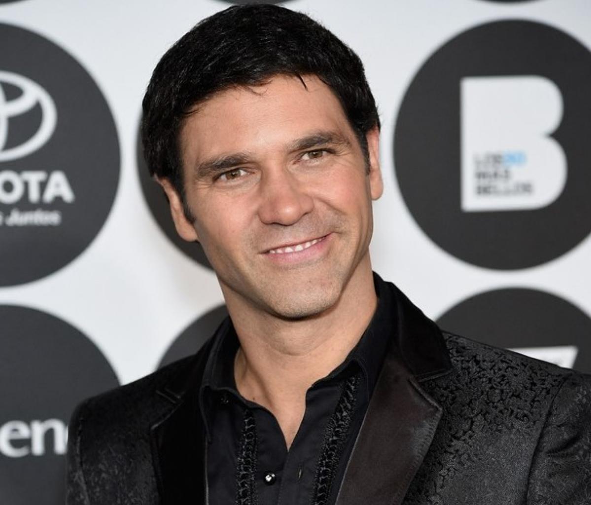 Valentino Lanús poartă o cămașă neagră și un sacou negru și zâmbește