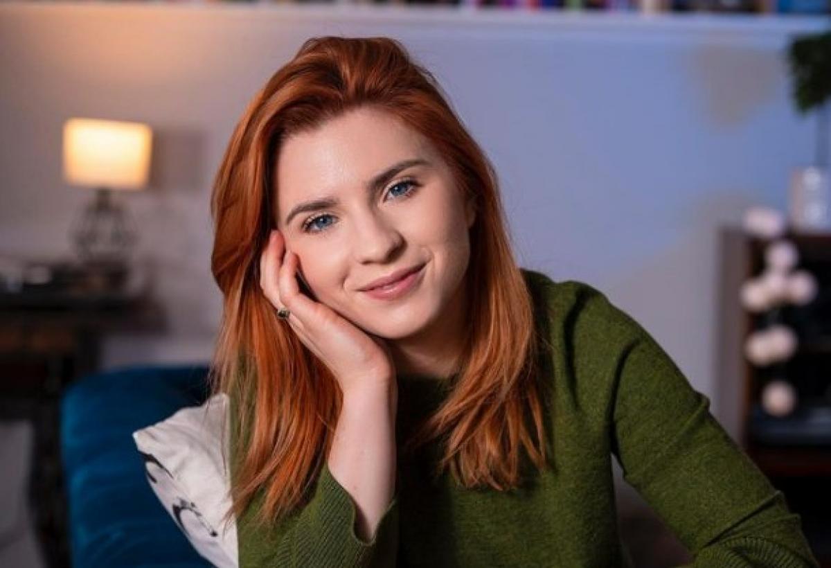 Cristina Ciobănașu poartă o bluză cu mânecă lungă și își ține mâna dreaptă la obraz