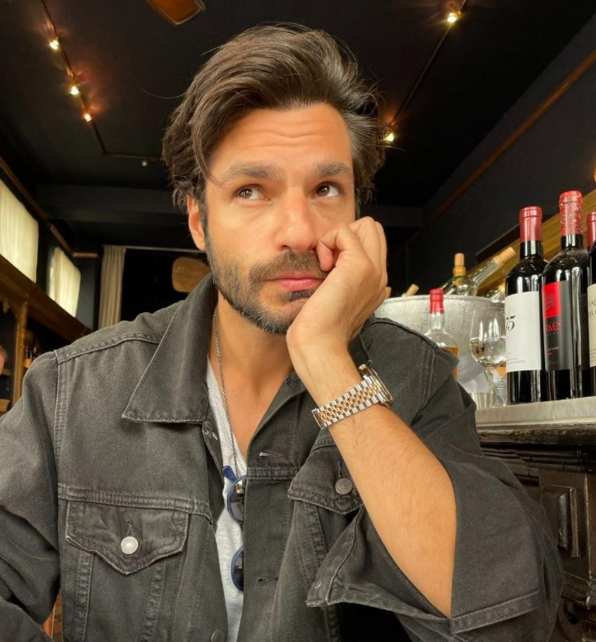 Serkan Çayoğlu poartă o cămașă cu mâneci lungi, ceas și își ține mâna stângă la obraz