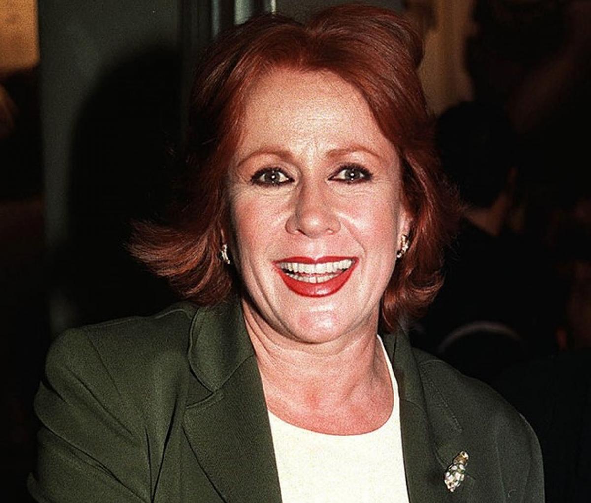 Laura Zapata poartă o bluză albă și un sacou verde închis și zâmbește