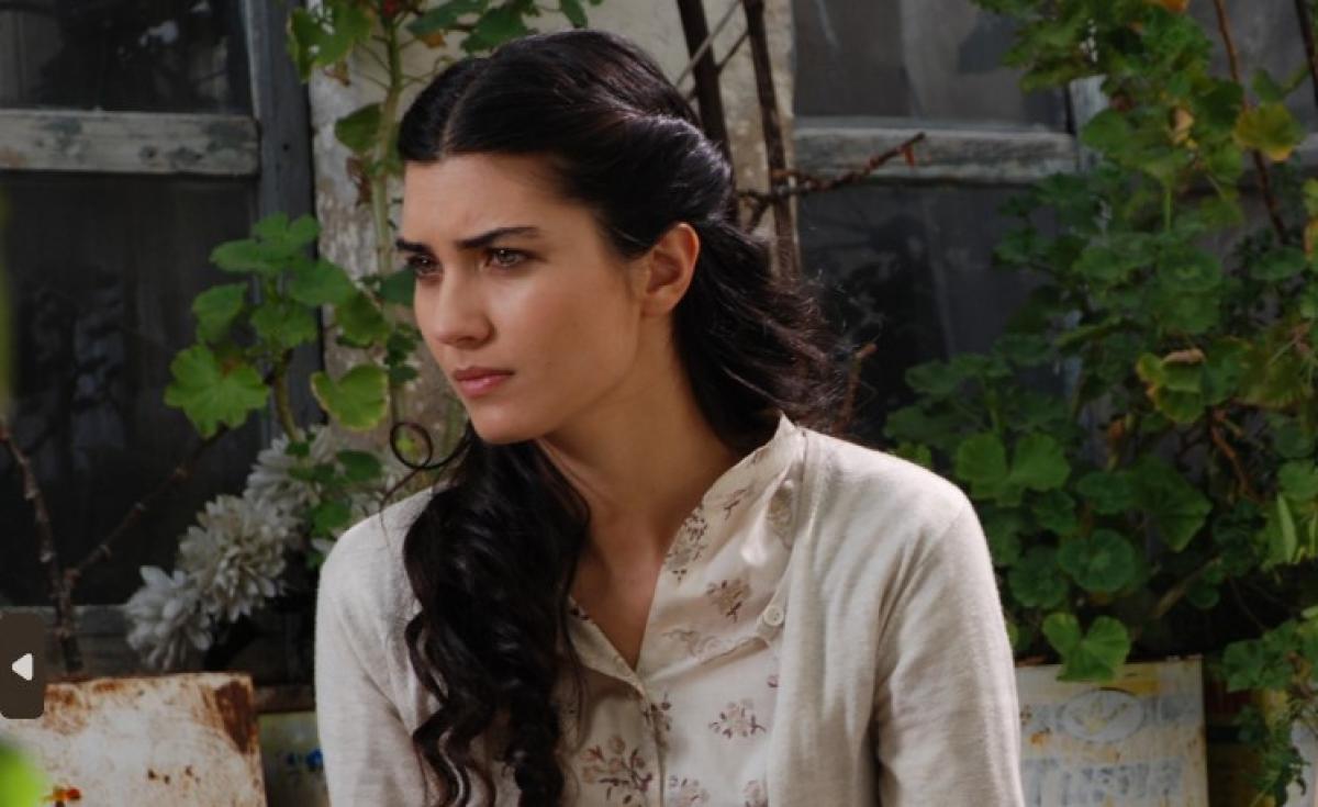 Tuba Büyüküstün poartă părul lung, desprins și o bluză cu mânecă lungă