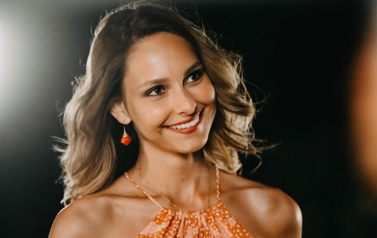 Jessica May poartă o bluză portocalie fără mâneci și zâmbește