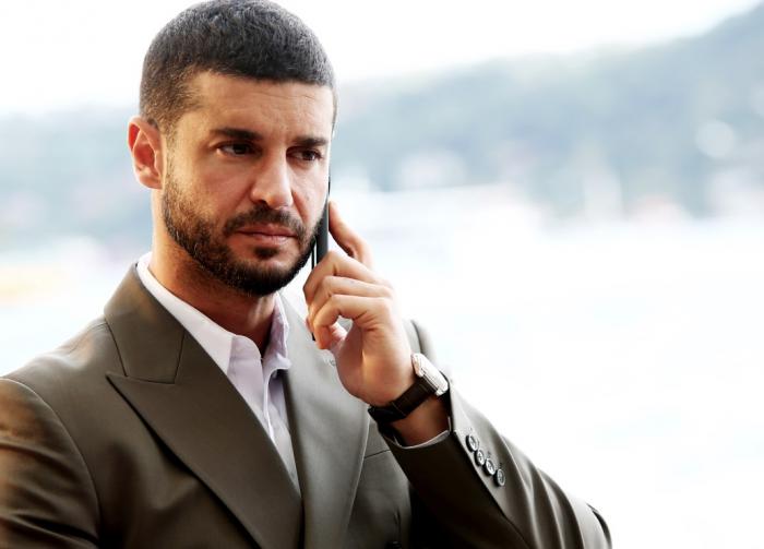 Berk Oktay poartă o cămașă albă și un sacou închis la culoare