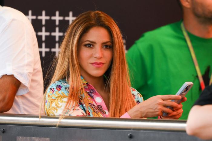 Shakira poartă o cămașă cu imprimeu, părul desprins și își ține telefonul în mâini
