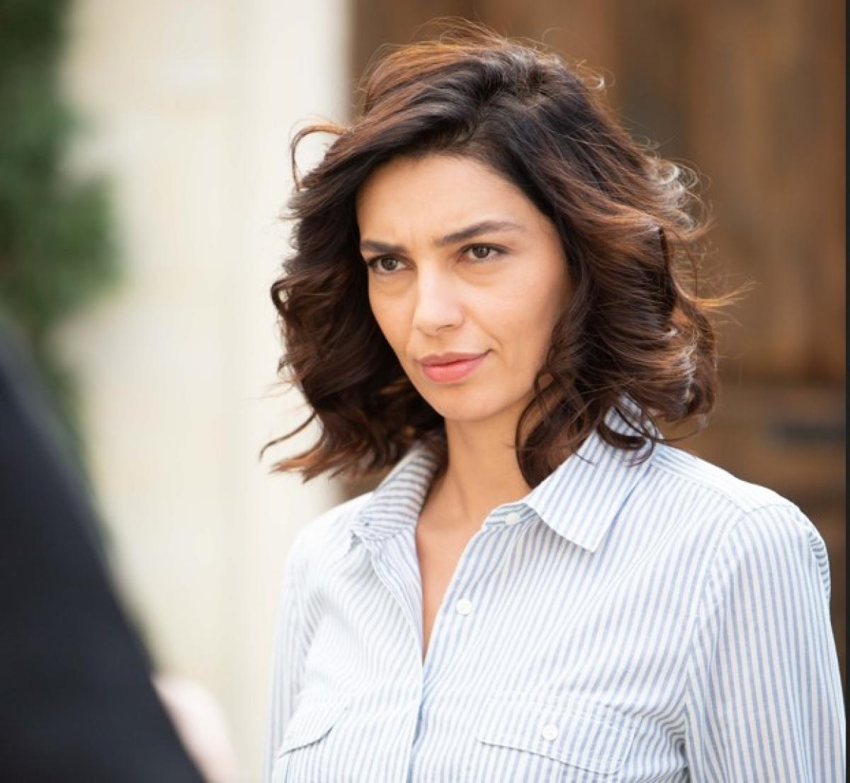 Ezgi Celik poartă o cămașă deschisă la culoare și are părul scurt, ondulat