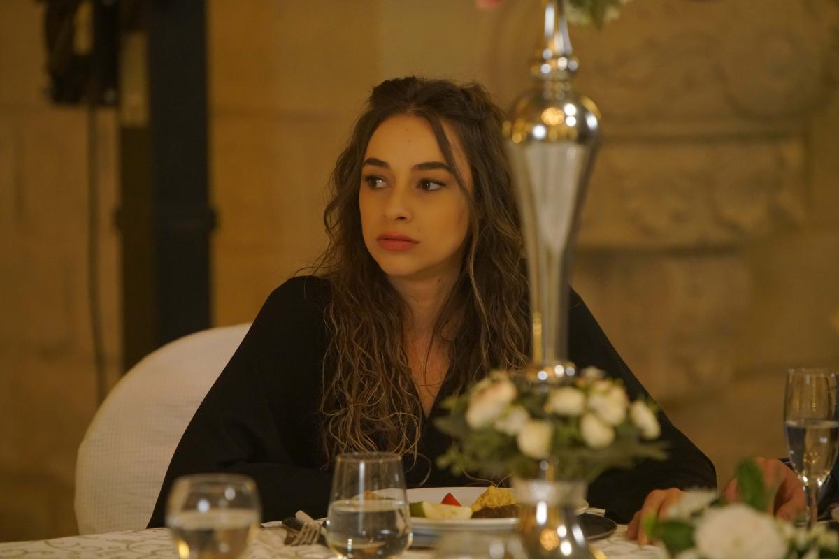 Hira Koyuncuoğlu poartă părul desprins și stă la masă