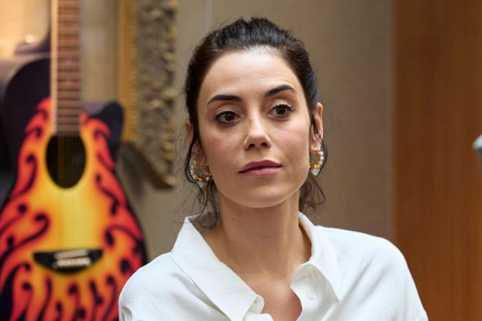 Cansu Dere poartă o cămașă albă cu mâneci lungi și are părul prins într-o coadă de cal