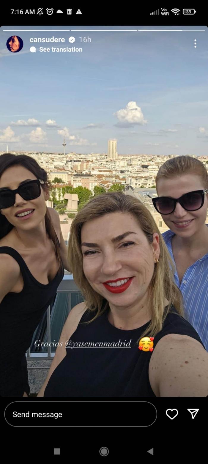 Cansu Dere poartă ruj roșu, rochie neagră fără mâneci și părul desprins și stă alături de două prietene