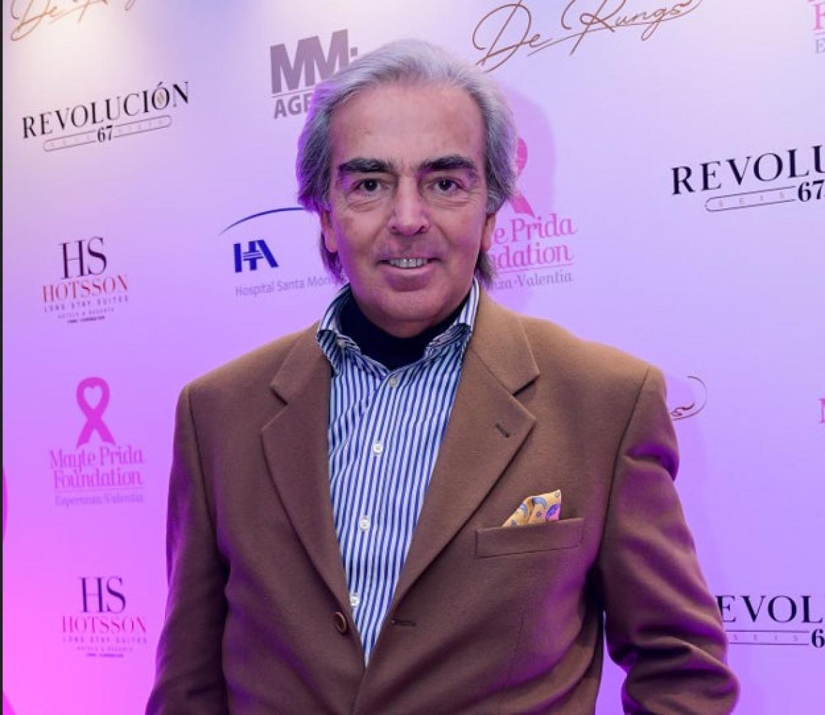 Lorenzo Lazo poartă o cămașă și un sacou maro și zâmbește