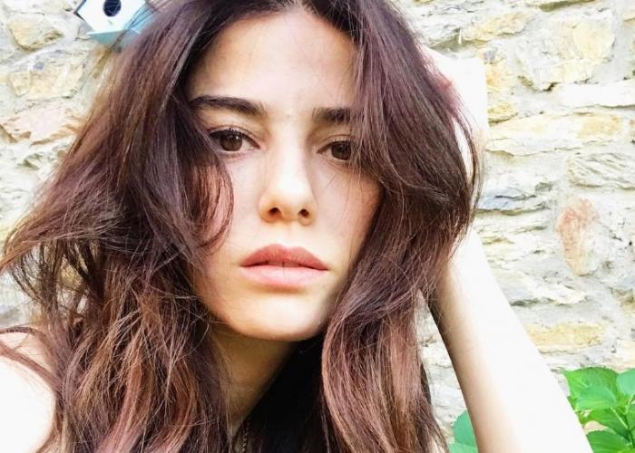 Özge Gürel poartă părul lung, desprins și își ține mâna stângă spre ureche