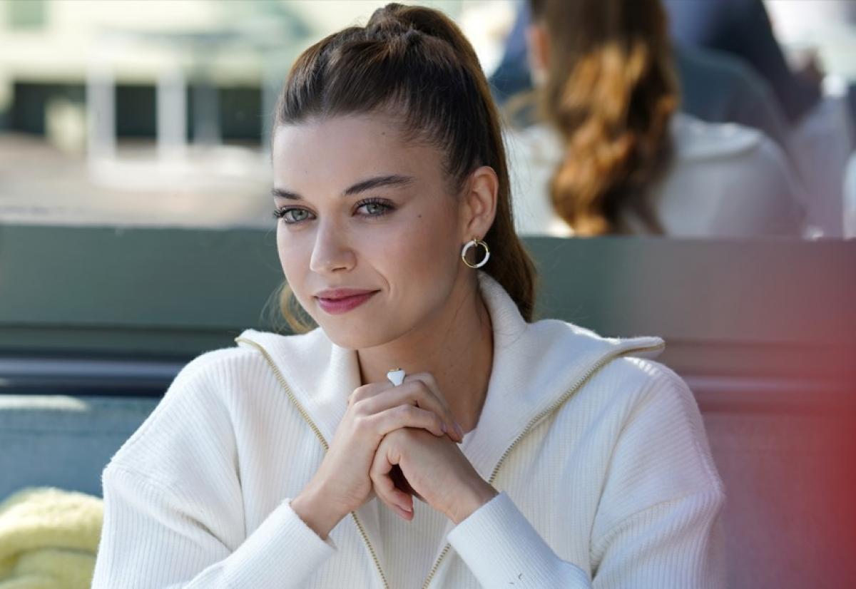 Afra Saraçoğlu poartă o cămașă albă cu mâneci lungi și are părul prins în coadă de cal